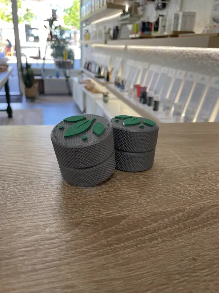 Petites boîtes moletées grises au couvercle orné d'un logo vert, sur un comptoir de boutique