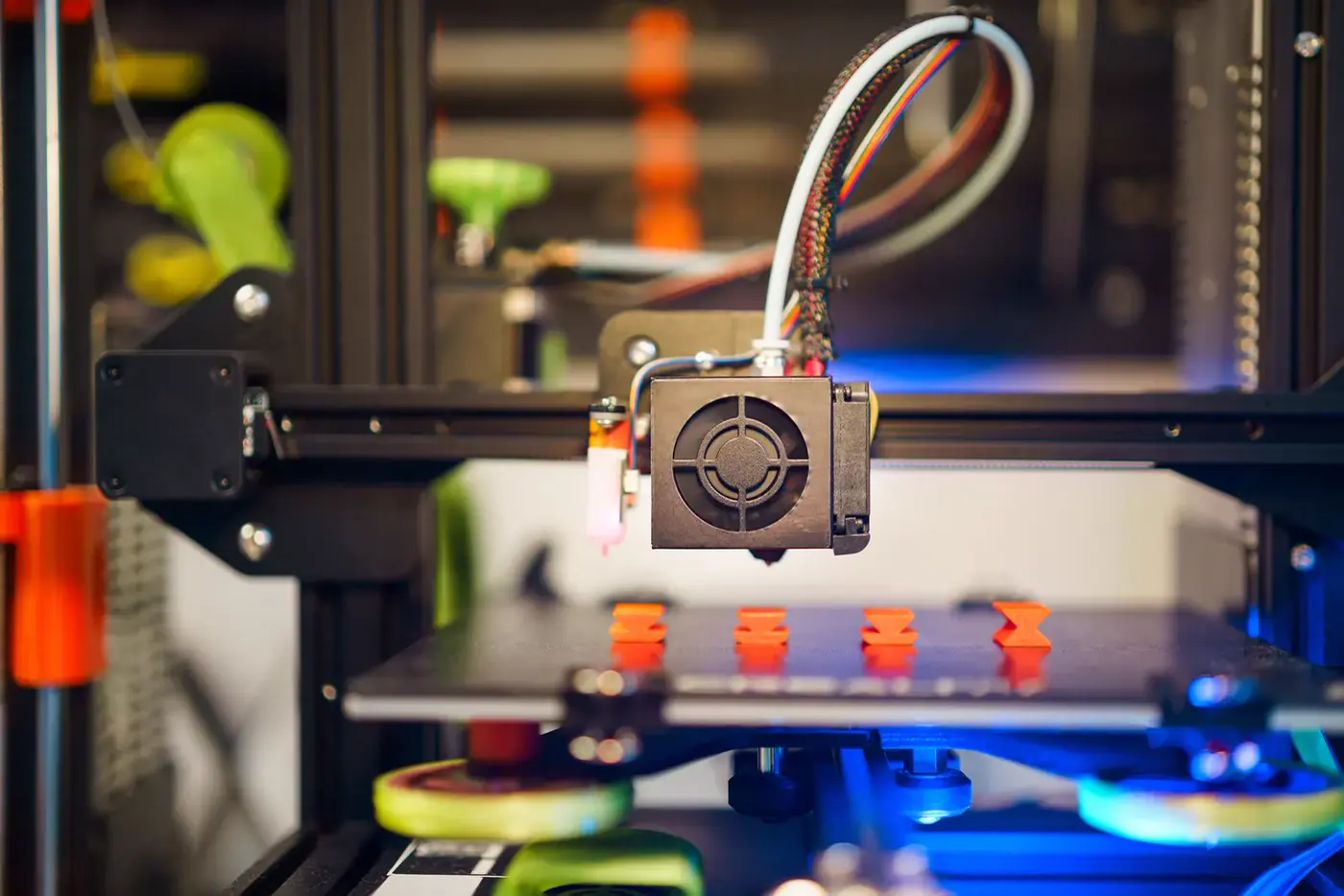 Imprimante 3D vue de face, quatre petites pièces orange posées sur son plateau