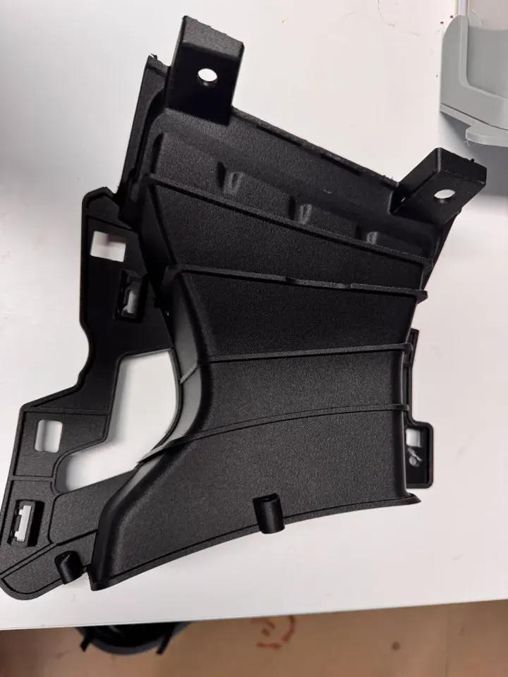 Pièce technique noire de carrosserie automobile, avec ses pattes de fixation, refaite sur mesure