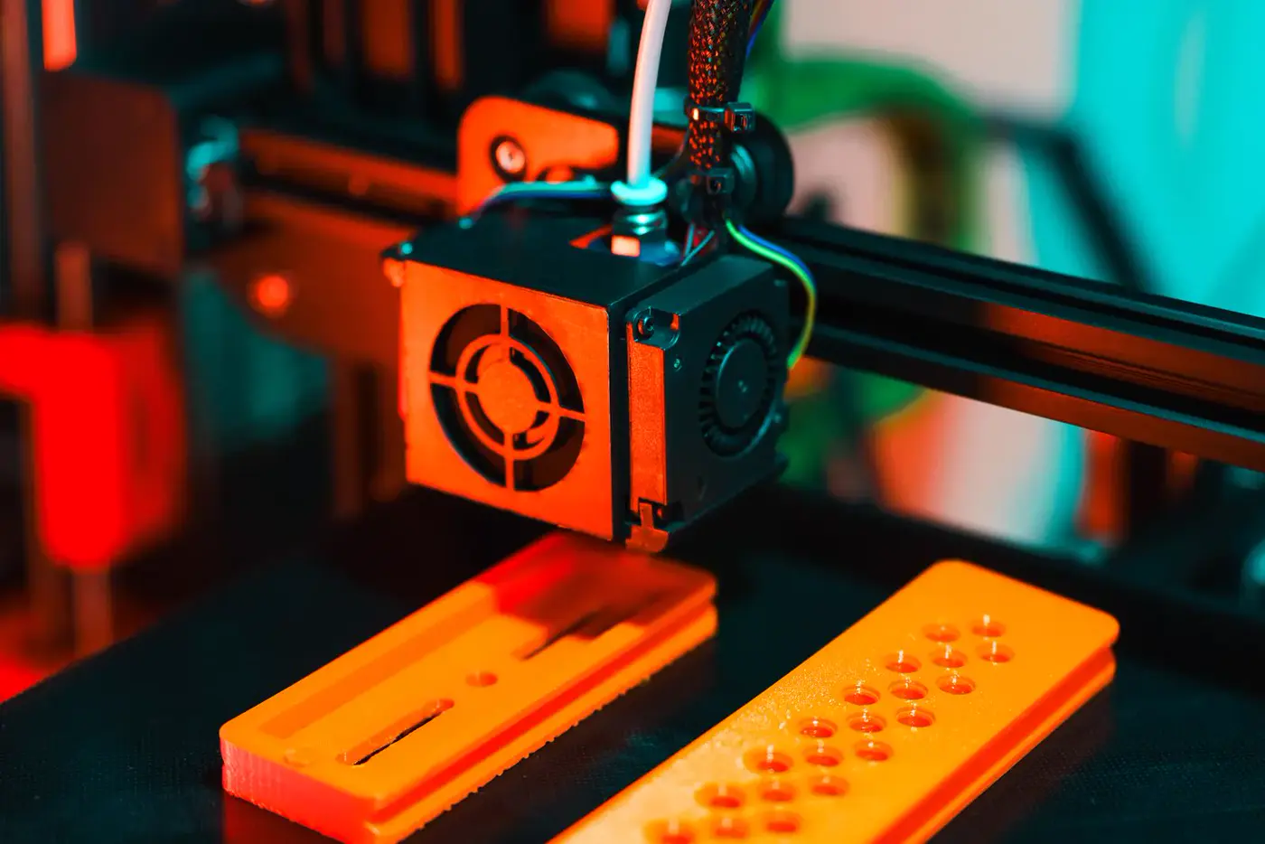 Tête d'une imprimante 3D au-dessus de deux pièces orange en cours d'impression
